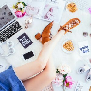 woman wearing brown open-toe chunky sandals sitting beside white smartphone, headphones and laptop