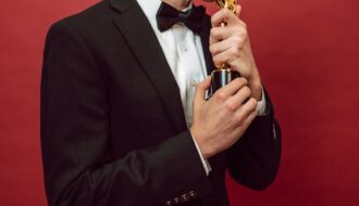 Man in a tuxedo kissing a trophy, symbolizing achievement, against a vibrant red background.