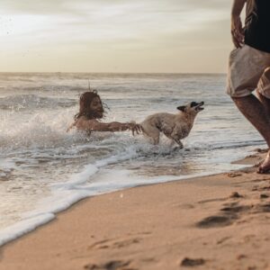 a man and a woman playing with a dog on the beach
