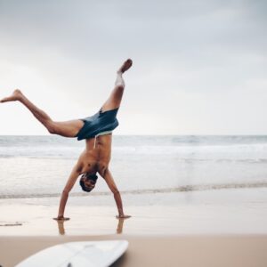 a man doing a handstand on a beach next to a surfboard