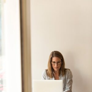 woman wearing grey striped dress shirt sitting down near brown wooden table in front of white laptop computer