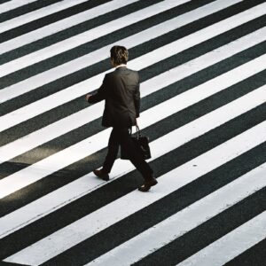 man in black formal suit jacket and pants carrying black bag while walking on pedestrian lane during daytime